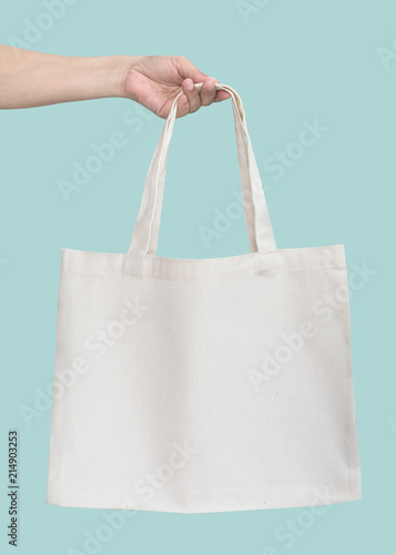 Tote bag canvas white cotton fabric cloth for eco shoulder shopping sack mockup blank template isolated on pastel green or blue mint background (clipping path) with woman’s handling hand