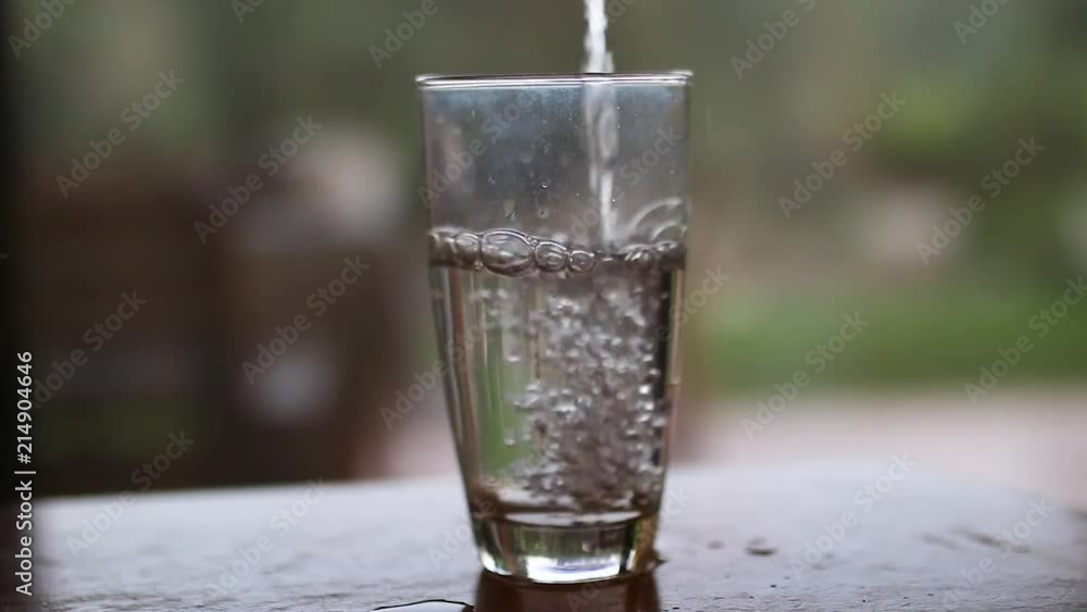 An empty glass filling up with water and then some ice is dropped in. An empty glass filling up with water and then some ice is dropped in.
