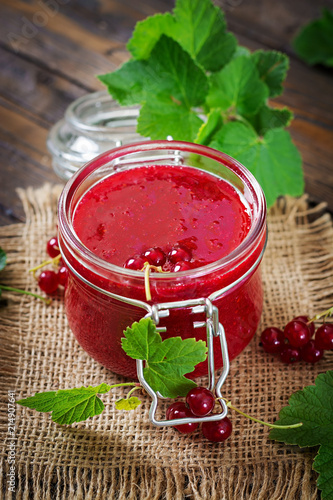 Red currant jam in a jar on a wooden background. Tasty food.