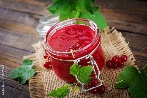 Red currant jam in a jar on a wooden background. Tasty food.