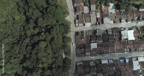 Aerial zenital drone shot over a car. Road centered, forest in one side, humble community in another side. photo