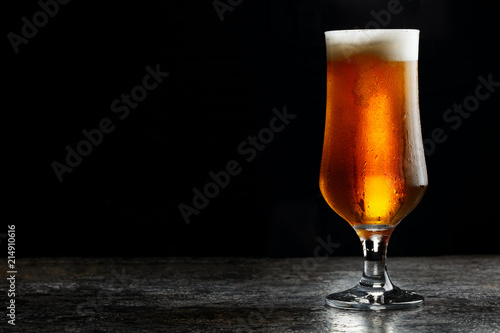 Glass of cold craft light beer on dark background..