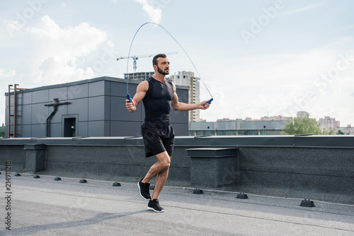 Canvas Print handsome sportsman training with jumping rope on roof