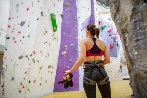 Photo from back of young woman athlete on background of wall for rock climbing
