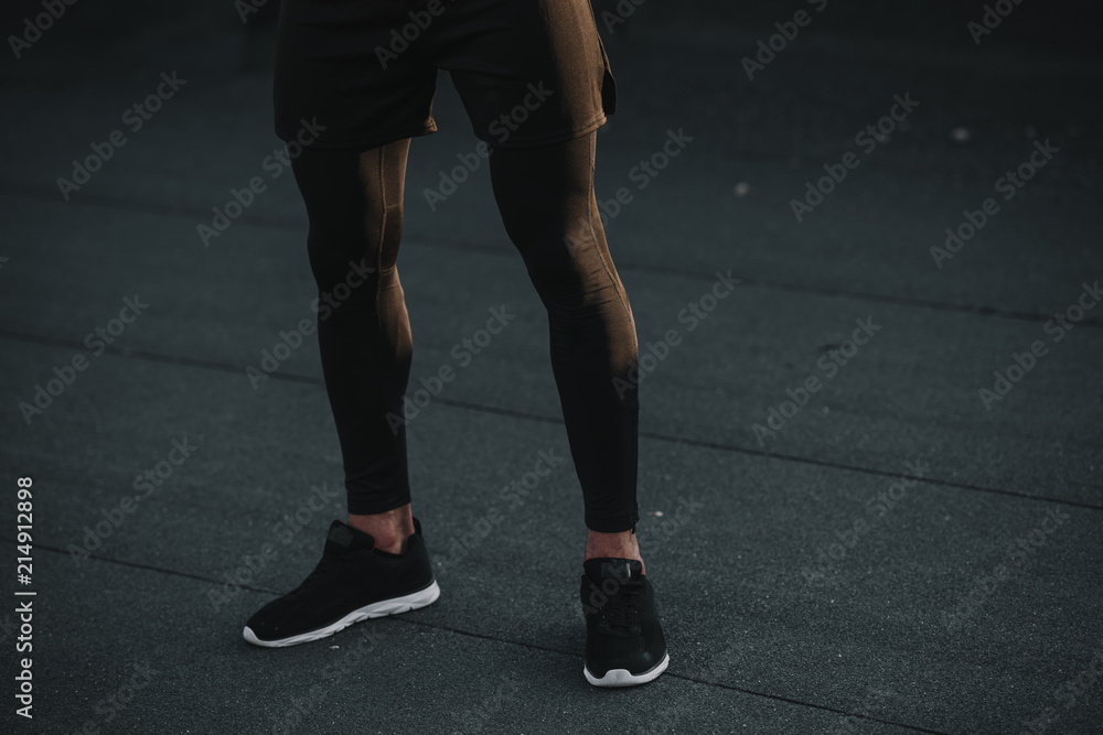 cropped image of sportsman standing in black sneakers and leggings on roof cropped image of sportsman standing in black sneakers and leggings on roof