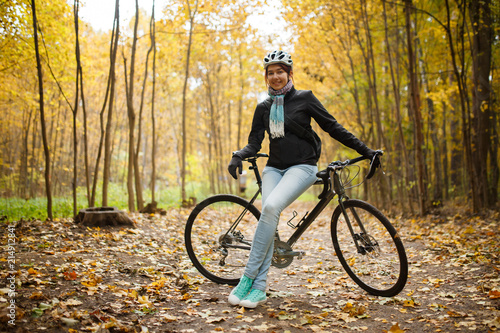 Picture of brunette in helmet, jeans next to bicycle in autumn park