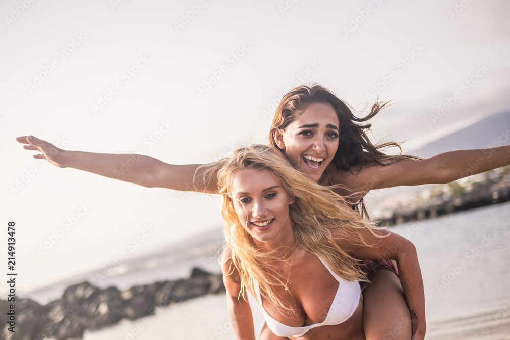 Naklejka premium happy young couple of females friends have fun together at the beach during summer vacation. outdoor leisure activity for beautiful model women enjoying the holiday. carrying on back.