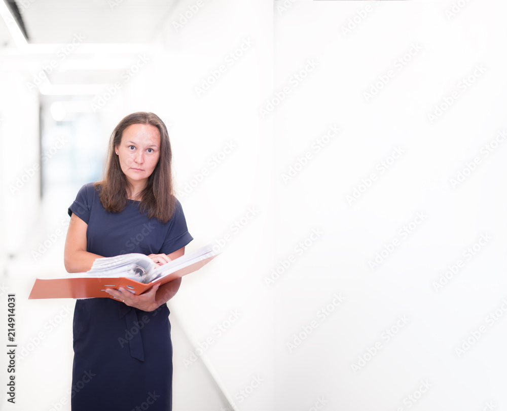 Portrait of confident beautiful middle age business woman holding orange folder in her hands standing on light background. Copyspace Portrait of confident beautiful middle age business woman holding orange folder in her hands standing on light background. Copyspace