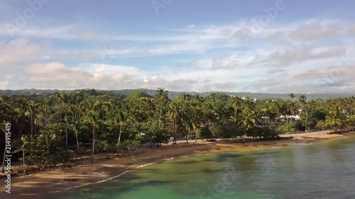 Areal shot of an empty beach in Samana Dominican Republic. Drone flighing downwards showing a beach with palm trees and a road in the background photo