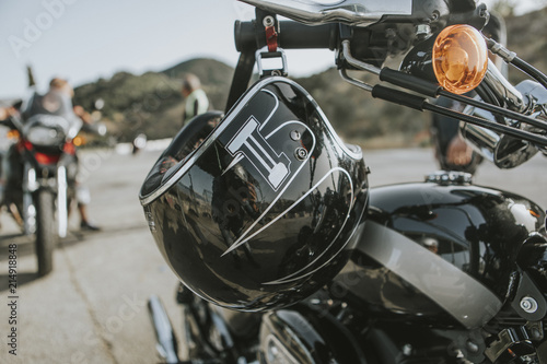 Close up of black helmet hanging from a classic black motorcycle handlebar.