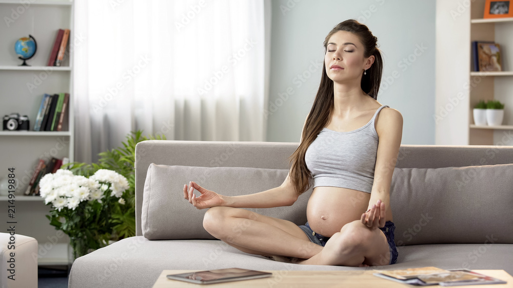 Pregnant woman meditating in lotus position, practicing yoga home for relaxation Pregnant woman meditating in lotus position, practicing yoga home for relaxation