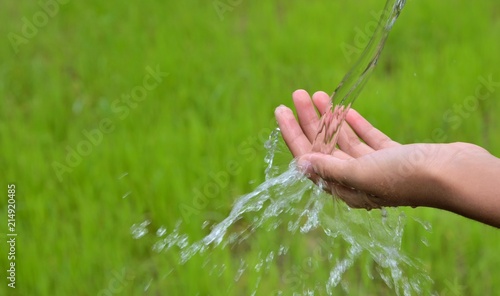 washing hand outdoors. Natural drinking water in the palm. Young hands with water splash, selective focus on green background concept.
