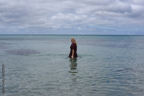 portrait of pretty blonde girl wearing purple dress, posing in a beautiful ocean landscape.