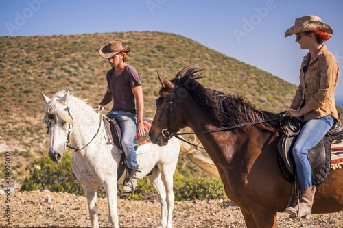 couple of rider man and woman with brown and white horses go and enjoy the outdoor leisure activity in excursion traveling the mountains. modern cowboy and no technology