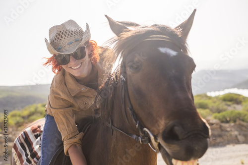 beautiful cheerful young woman enjoy and ride her brown cute horse in friendship and relationship. animal lover and pet therapy concept. travel and vacation alternative lifestyle