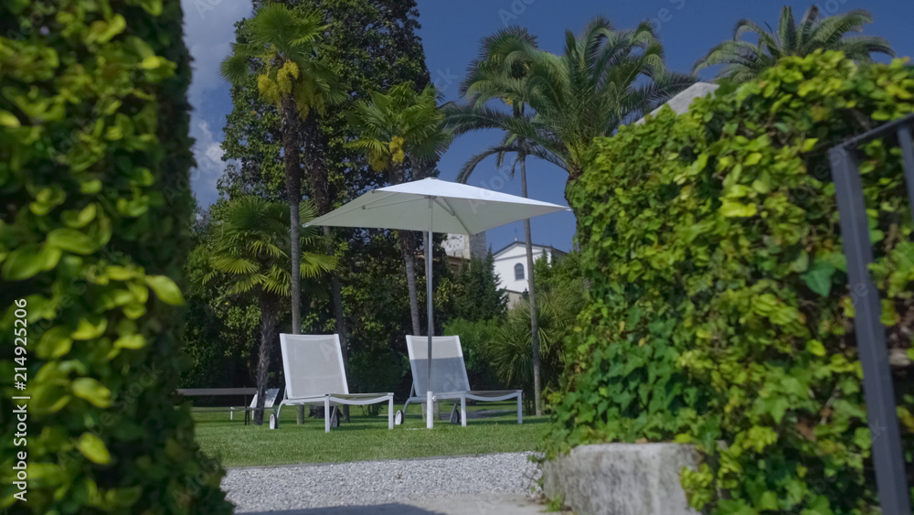 White sunbeds and sunshade standing in garden of private house, summer relax White sunbeds and sunshade standing in garden of private house, summer relax