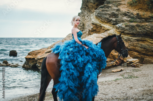  girl in a lush blue dress on a horse by the sea, beautiful blonde with blue eyes, summer, sadness