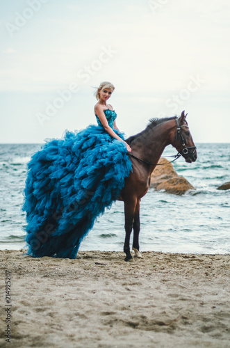  girl in a lush blue dress on a horse by the sea, beautiful blonde with blue eyes, summer, sadness