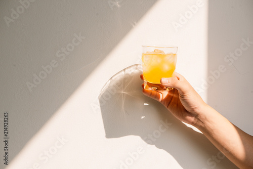 Hand holding full glass of orange juice in the morning in summer