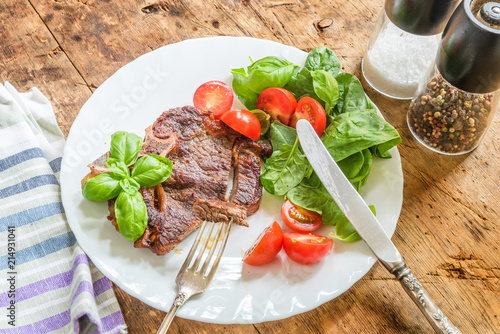Delicious fried steak with fresh salad of spinach and cherry tomatoes in a white plate on a rustic table
