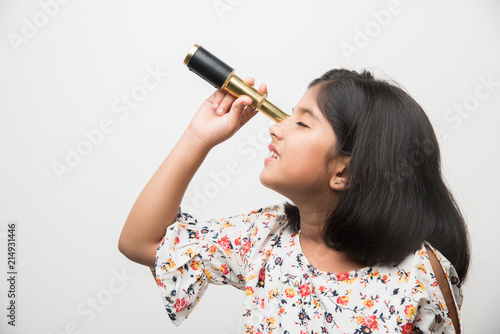 Cute little Indian/asian girl using stretch telescope and looking up in the sky, want to be a scientist. Standing isolated over white or green chalkboard background