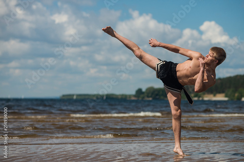 Kickboxer kicks in the open air in summer against the sea.
