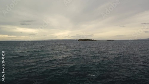 Flying over the sea on a cloudy day. Small island on the horizon. photo