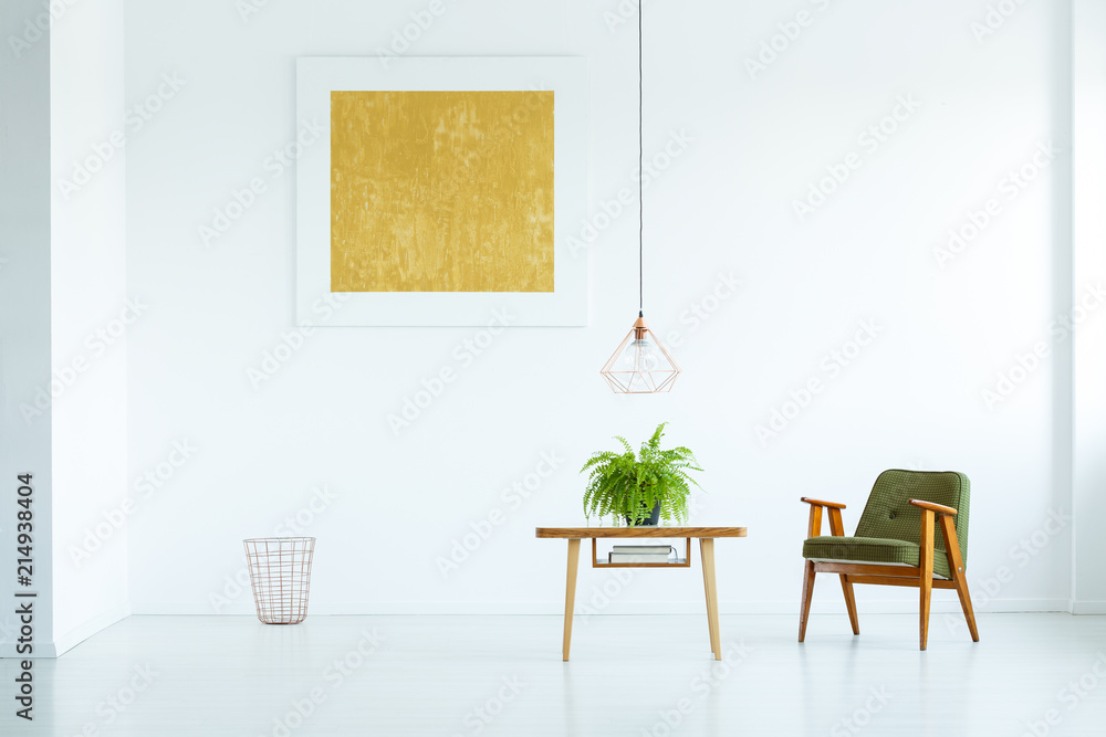 Fototapeta premium Lamp above table with fern next to green armchair in white interior with yellow painting. Real photo