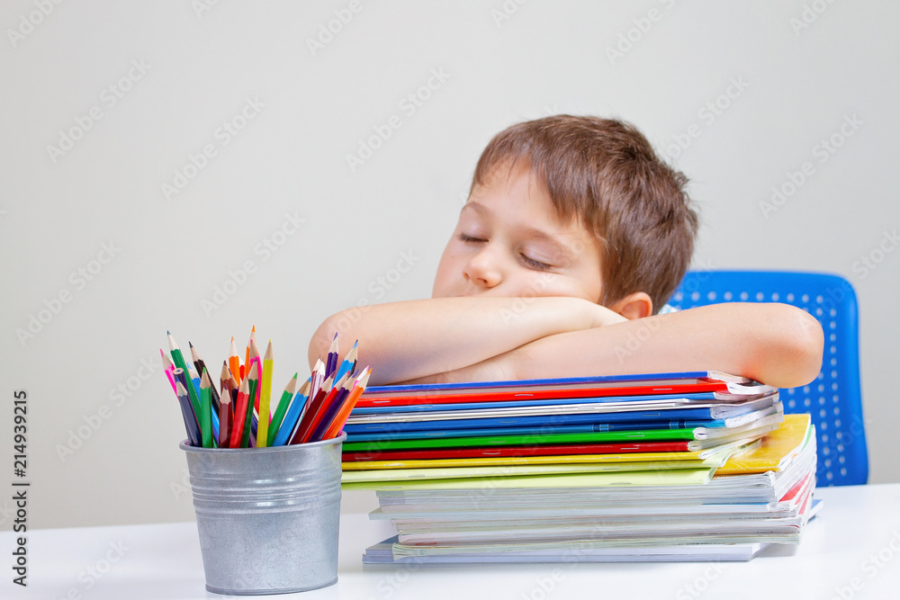 Tired school boy sleeps sitting at the table with big pile of books, textbooks and notebooks Tired school boy sleeps sitting at the table with big pile of books, textbooks and notebooks