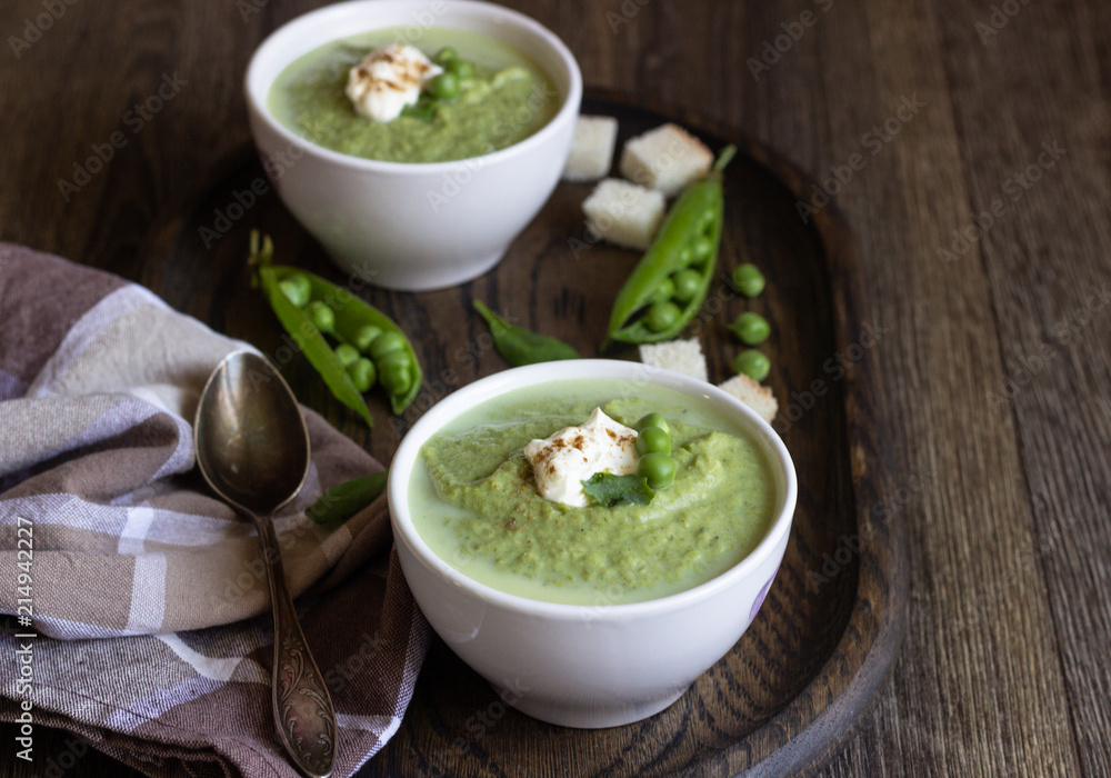 Green pea soup in bowls with spinach and cream on wooden rustic cutting board. Green pea soup in bowls with spinach and cream on wooden rustic cutting board.