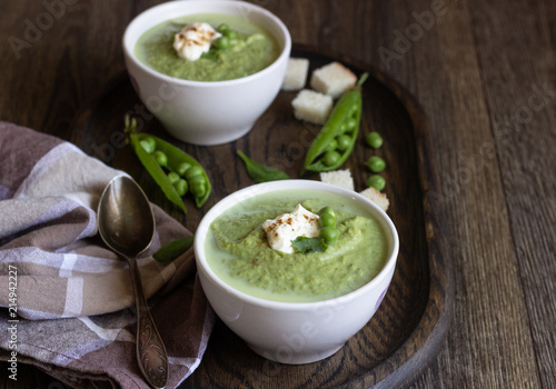 Green pea soup in bowls with spinach and cream on wooden rustic cutting board.