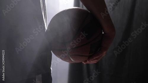 Close footage of basketball player holding ball, standing in dark misty room