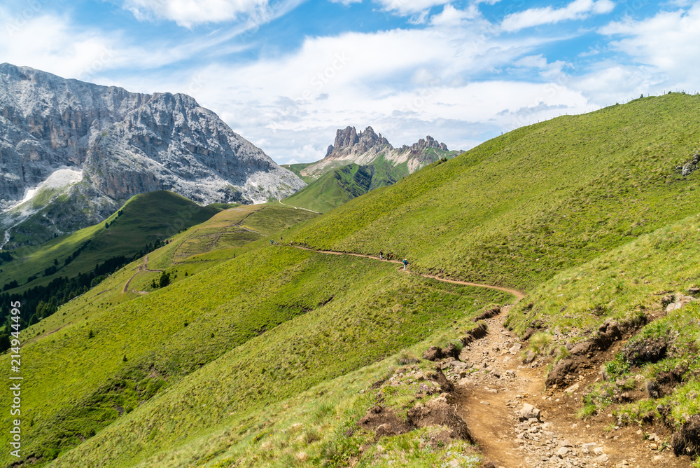 Naklejka premium Italian Dolomites Landscape. Light after rain in Dolomites. Rocky peaks in the background surrounded by rain clouds. Mountain valley with layers of forest and mountains. Aerial view path trail hikeing