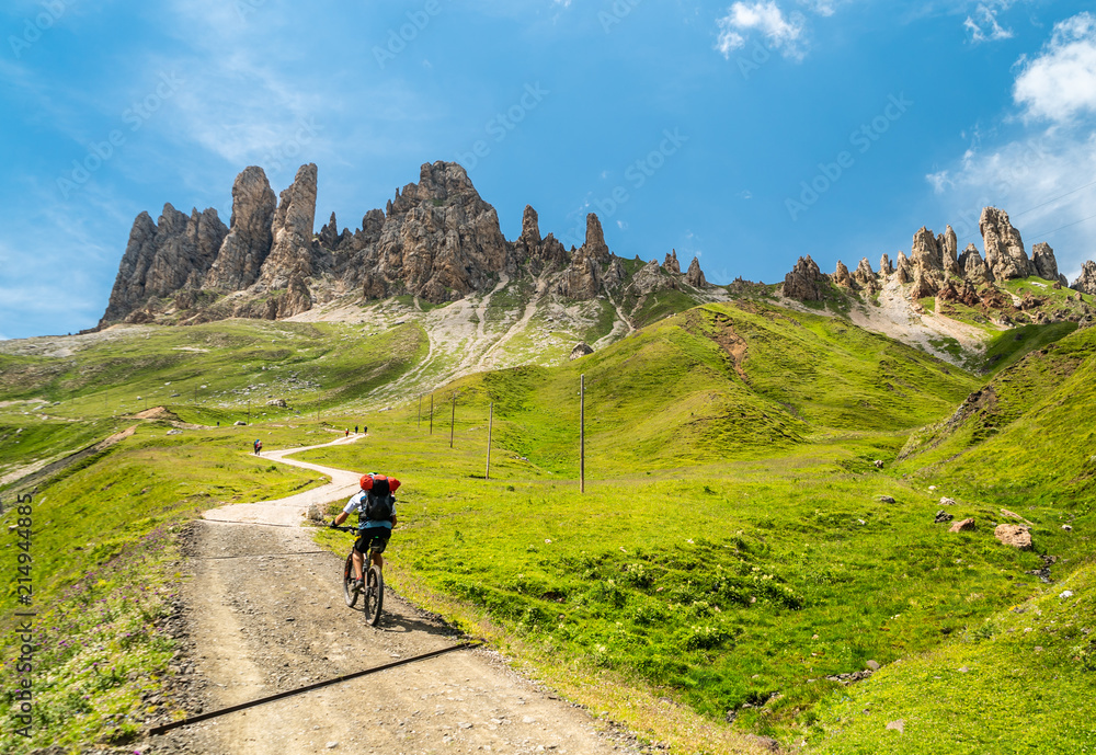 Alpine activities in Dolomites,Italy. Mountainbiking uphill on the Mountain Road in Dolomites Mountains. Rocky Mountains Ridge in the background. Cycling with bikes on track, Cortina d'Ampezzo