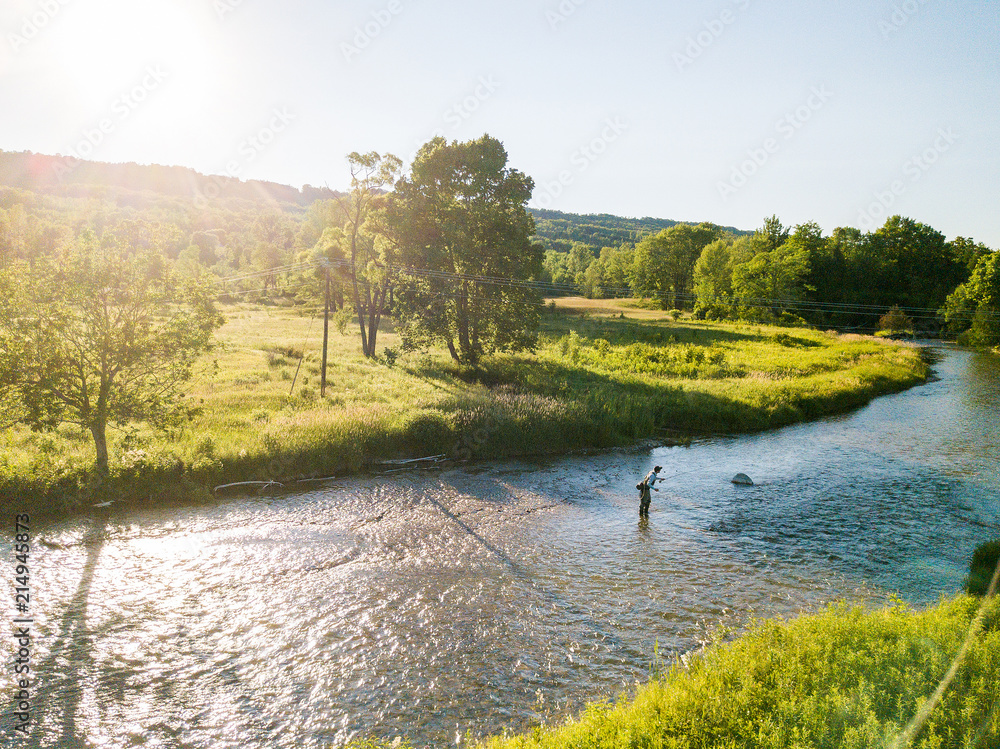Drone aerial shot of a man fly fishing in the summer in a river