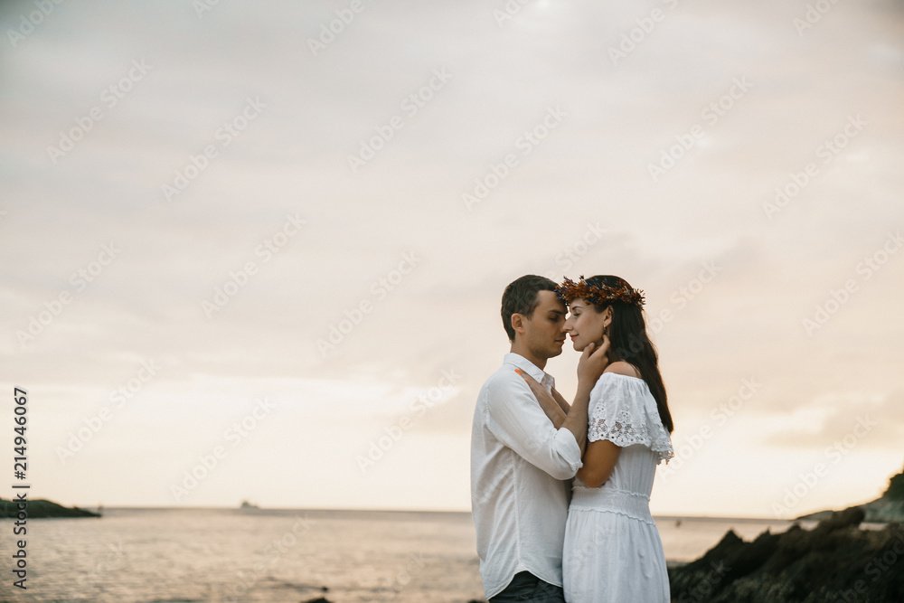 A loving couple in white clothes hugs against the background of the tropical sky, the sea and the shore. Rest for two.