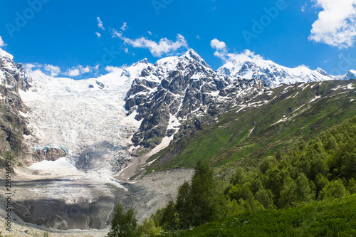 Adishi glacier with blue sky on background and green trees on foreground in Georgia, Svaneti region photo