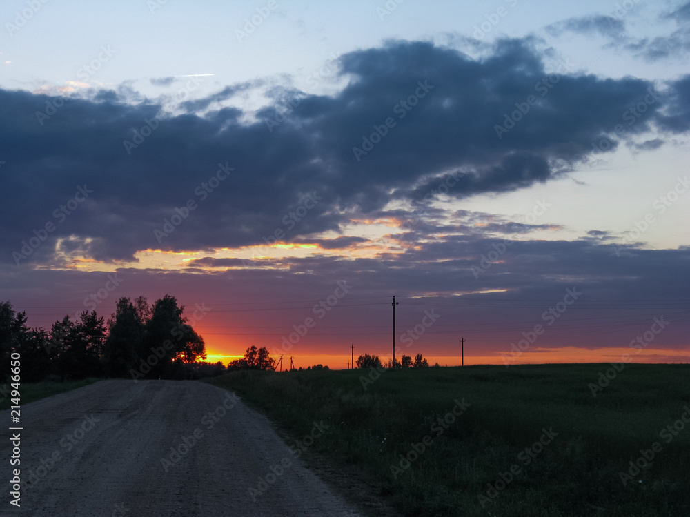 Fototapeta premium A bright orange sunset against the background of fields with grains