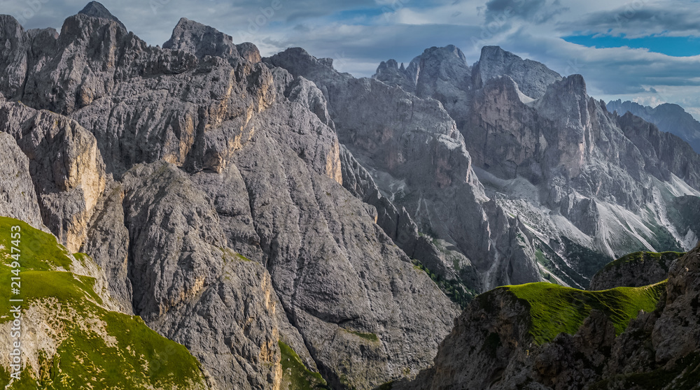 Fototapeta premium Landscape of Dolomites with green meadows, blue sky, white clouds and rocky mountains. Italian Dolomites landscape. Beauty of nature concept background. The valley below. Evening panoramic view. 