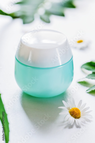container with cosmetic on white background with field flowers and leaves. The concept of summer and idea for advertisement of cream. Flatlay.