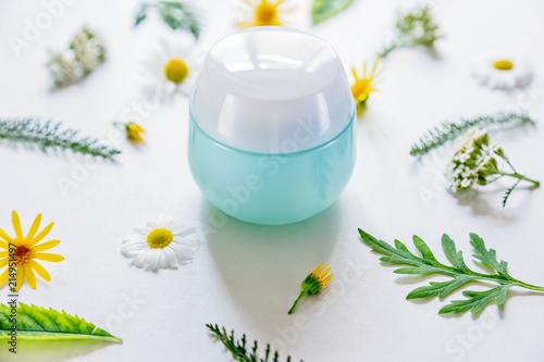 container with cosmetic on white background with field flowers and leaves. The concept of summer and idea for advertisement of cream. Flatlay.