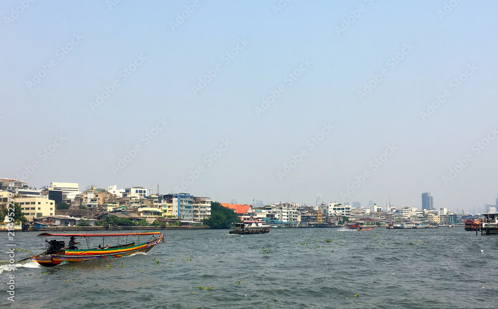 Colorful Thai longtail sightseeing boat on the Chao Phraya River with cityscape background in windy and cloudy day in Bangkok, Thailand