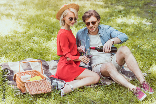 boyfriend pouring red wine in glasses at picnic in park