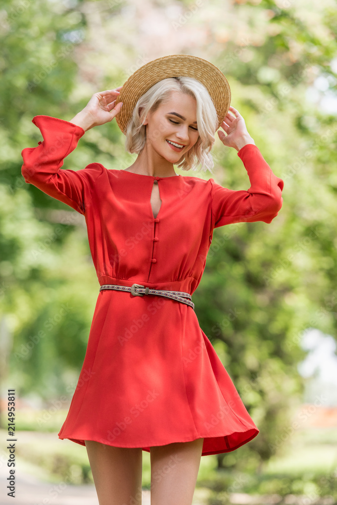 Obraz premium stylish attractive girl in red dress and straw hat posing in park