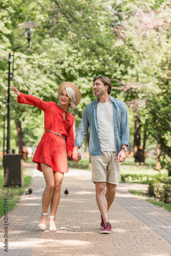 Fototapeta Naklejka Na Ścianę i Meble -  happy girlfriend and boyfriend walking together in park and holding hands
