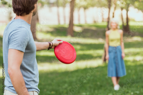 Foto young couple playing frisbee with red frisbee disk in park