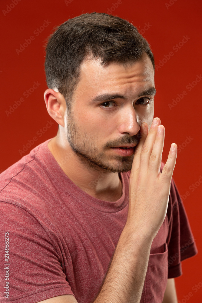 Fototapeta premium The young man whispering a secret behind her hand over red background