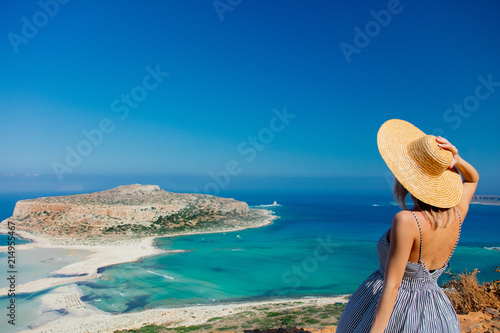 Fotografie Young redhead girl in hat and dress with sea coastline on Balos, Crete, Greece