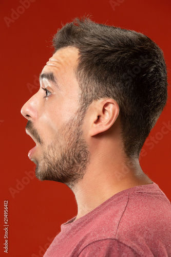 The young attractive man looking suprised isolated on red