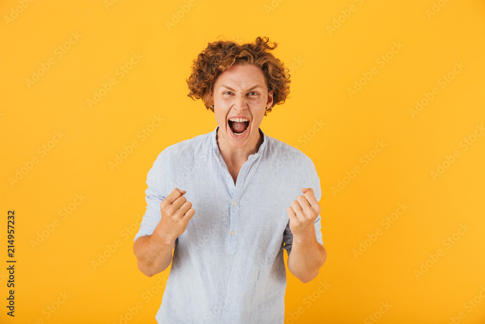 Portrait of surprised cheerful man 20s screaming and clenching fists, isolated over yellow background Portrait of surprised cheerful man 20s screaming and clenching fists, isolated over yellow background